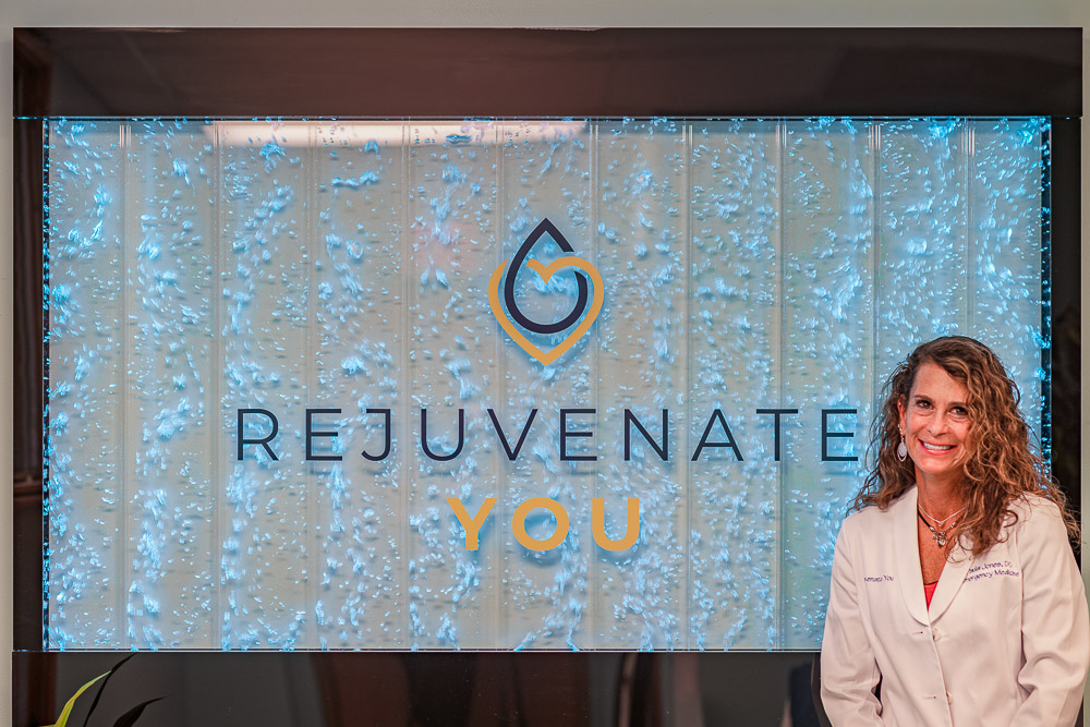 Dr. Paula Jones smiling in front of a Rejuvenate You sign.