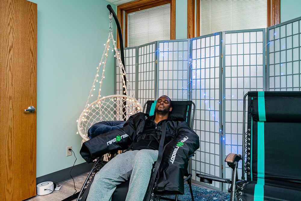 Man relaxing with his eyes closed while using NormaTec arm compression units. 