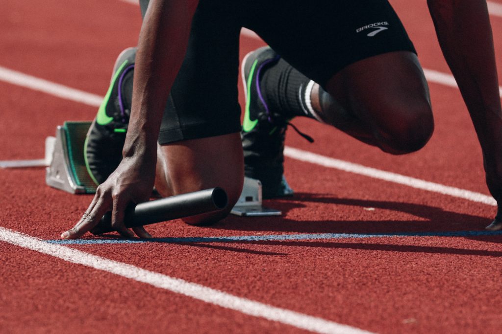 Relay runner on a track poised with baton in hand for the starter gun.