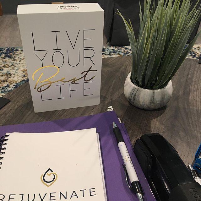 A desk with a pen, a plant, a decoration that says "Live Your Best Life," and a Rejuvenate You binder.