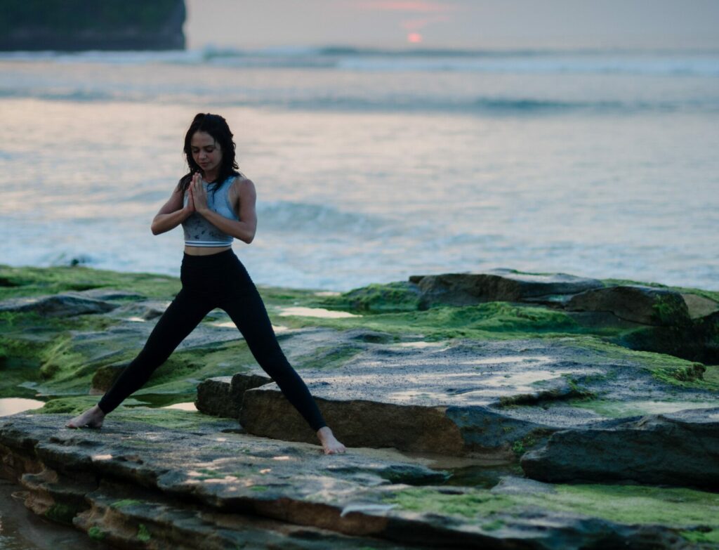 A woman performing a yoga pose on some rocks by the water.