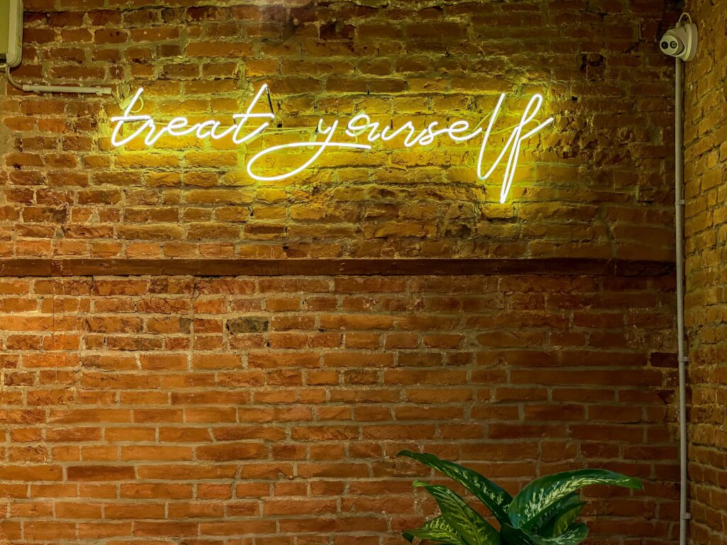 Neon yellow script that says "treat yourself" on a brick wall.