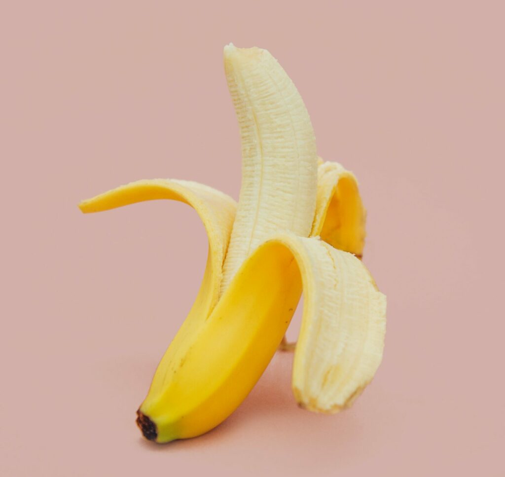 A peeled banana against a light pink background.