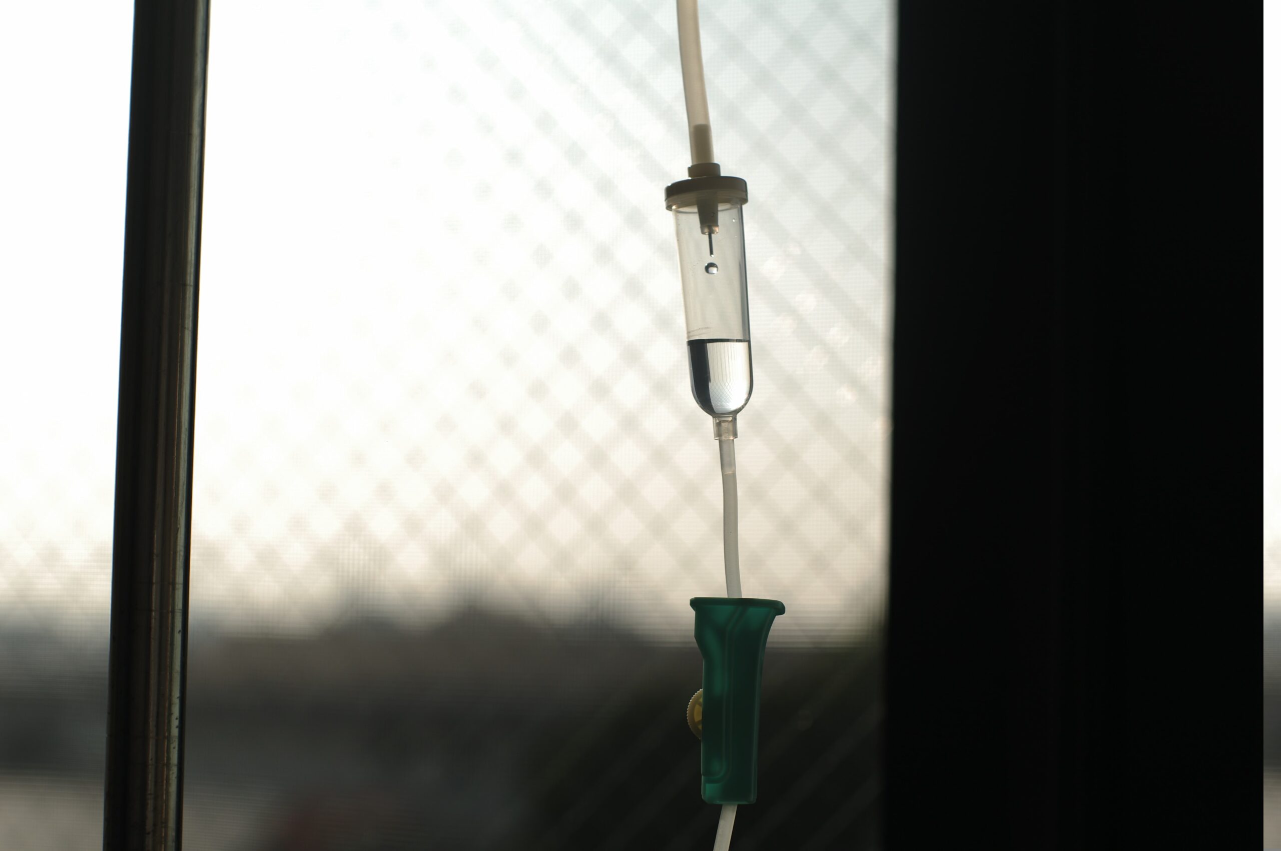 A liquid IV drips into a bag by a window.