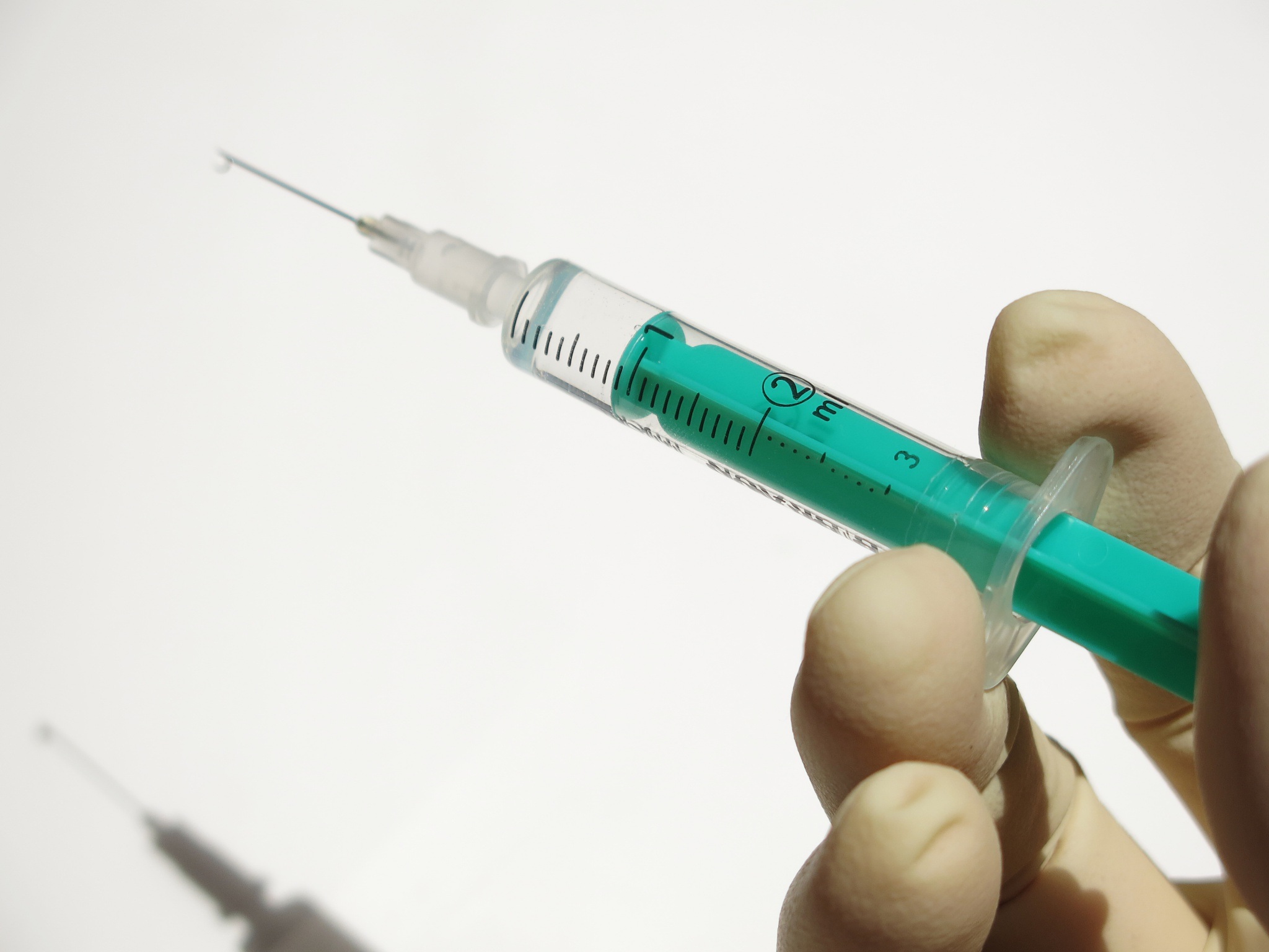 A latex gloved hand holding a syringe with a green plunger rod.