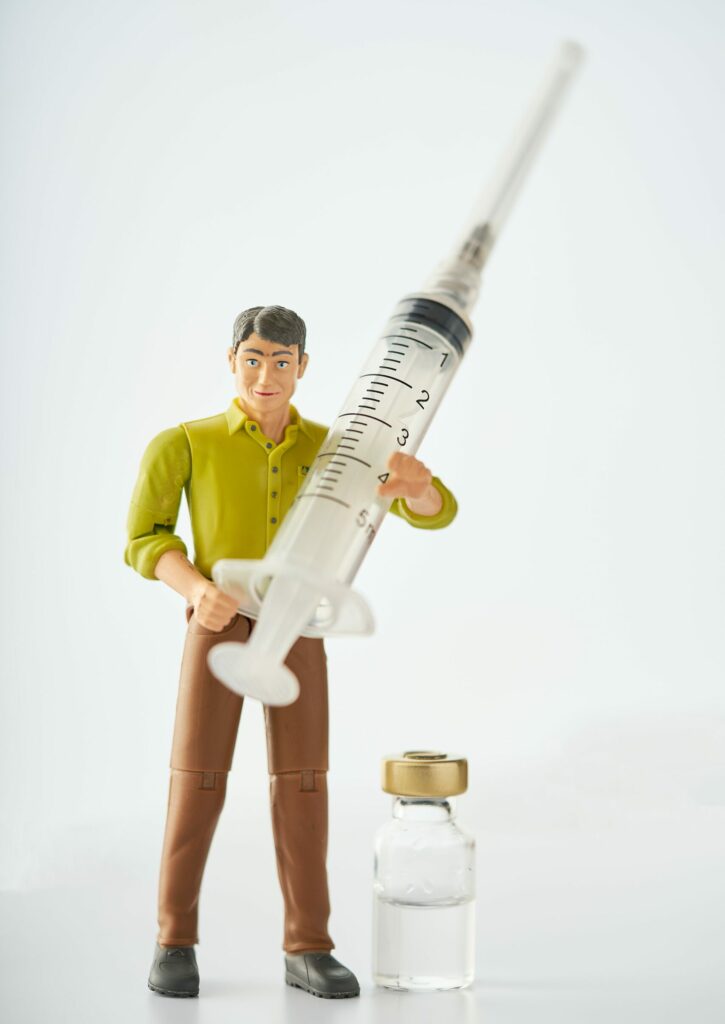 A small toy man is holding a large syringe and standing beside a vial of some solution.