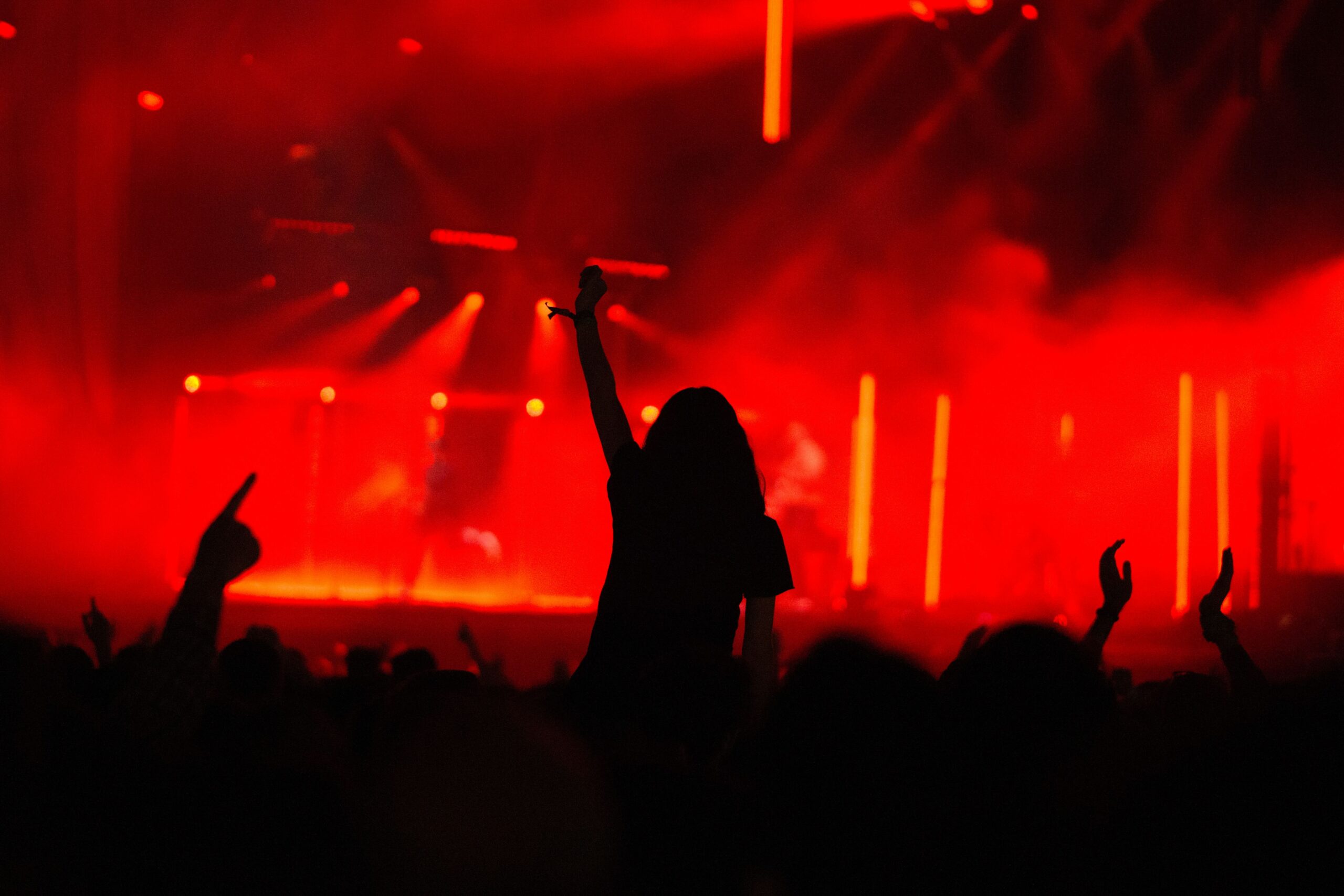 The silhouette of a crowd raising their hands and cheering at a stage with red lights.