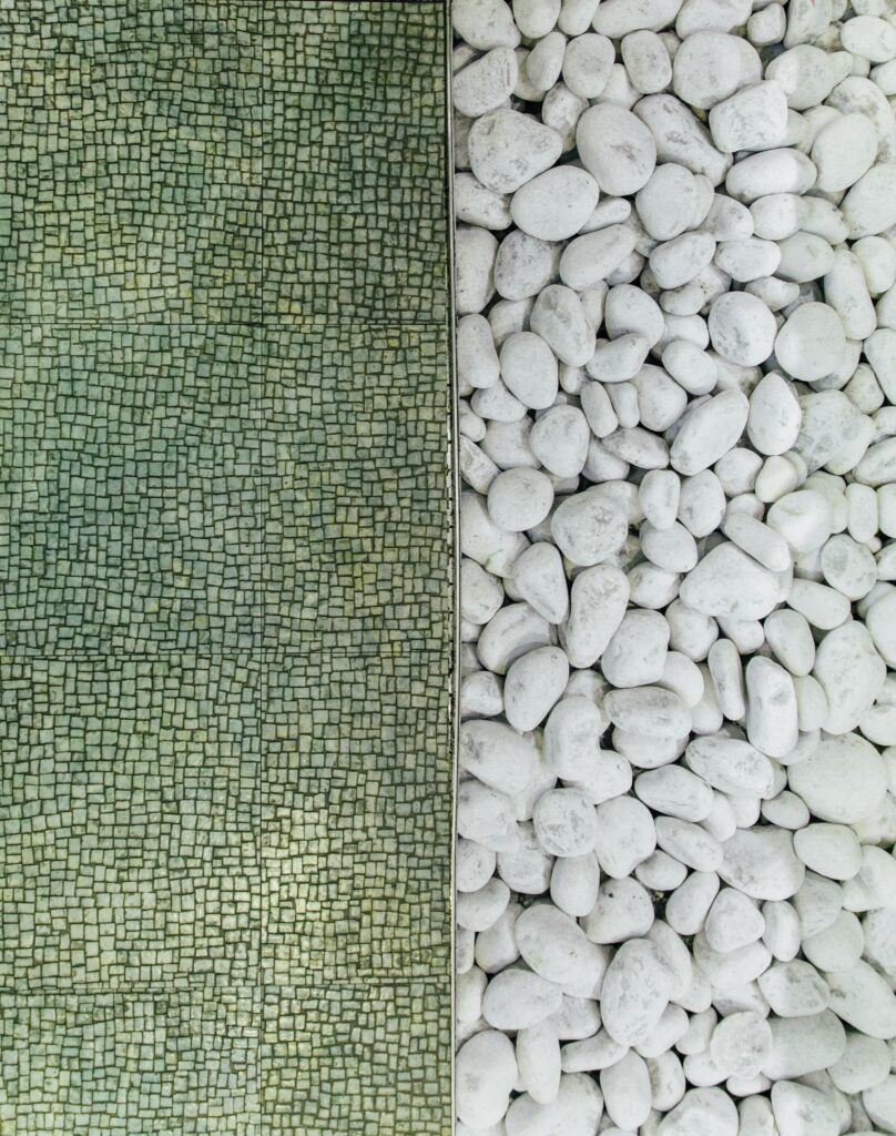 A barrier bisects smooth, white stones on one side and a varied, green texture on the left.