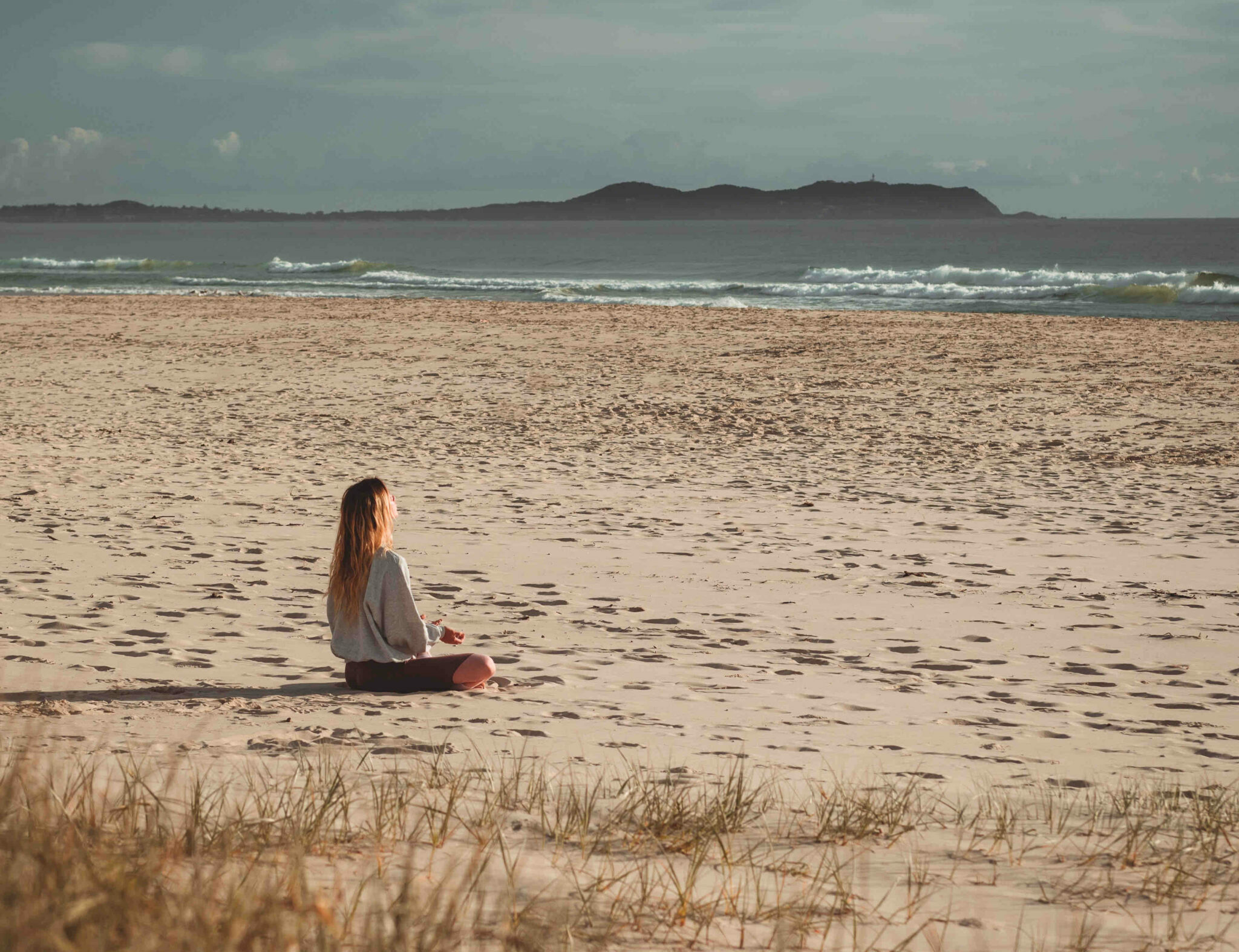 A girl meditating on an empty beach.