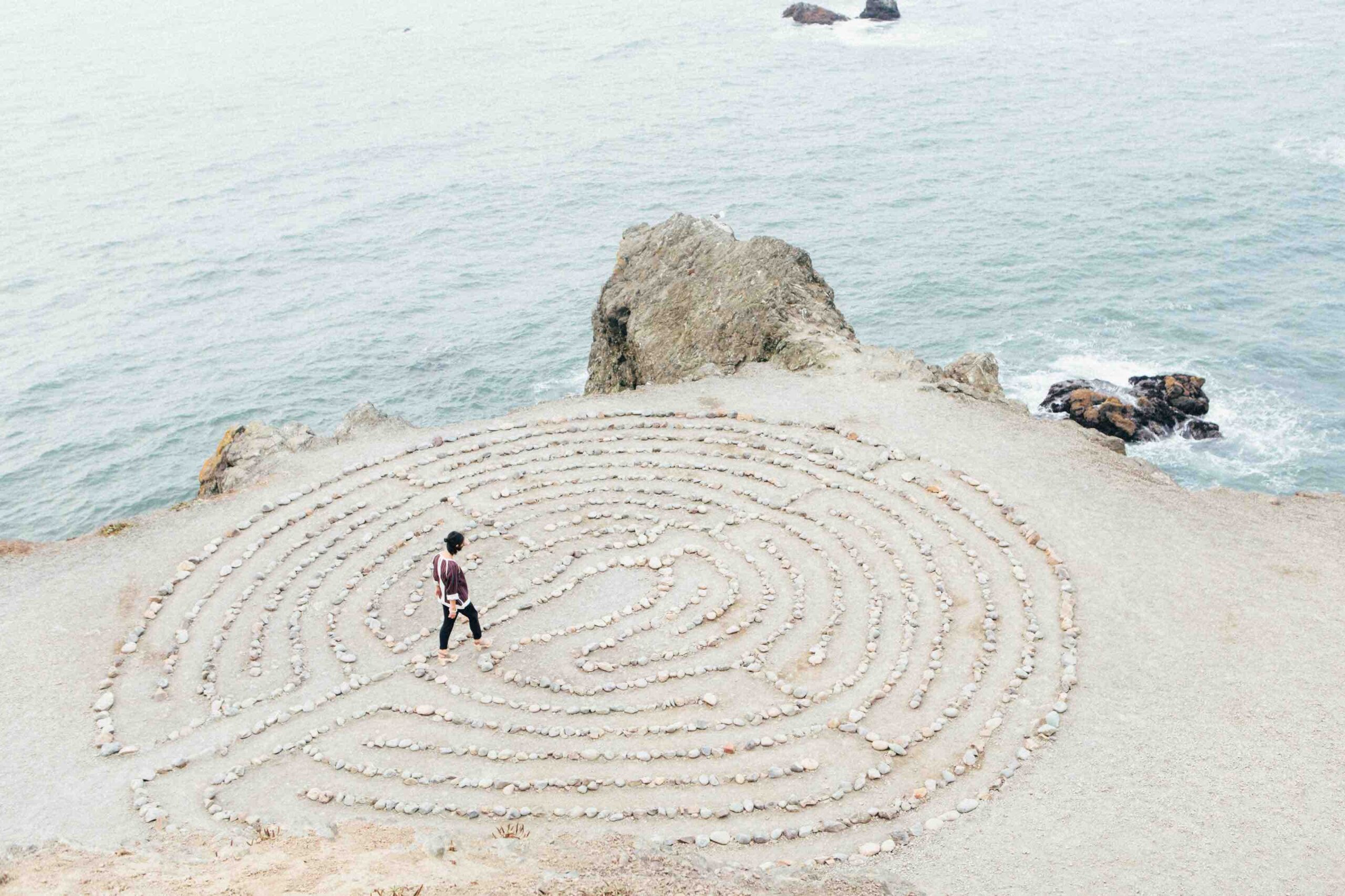 A man walking to the center of a circular drawing in the sand.