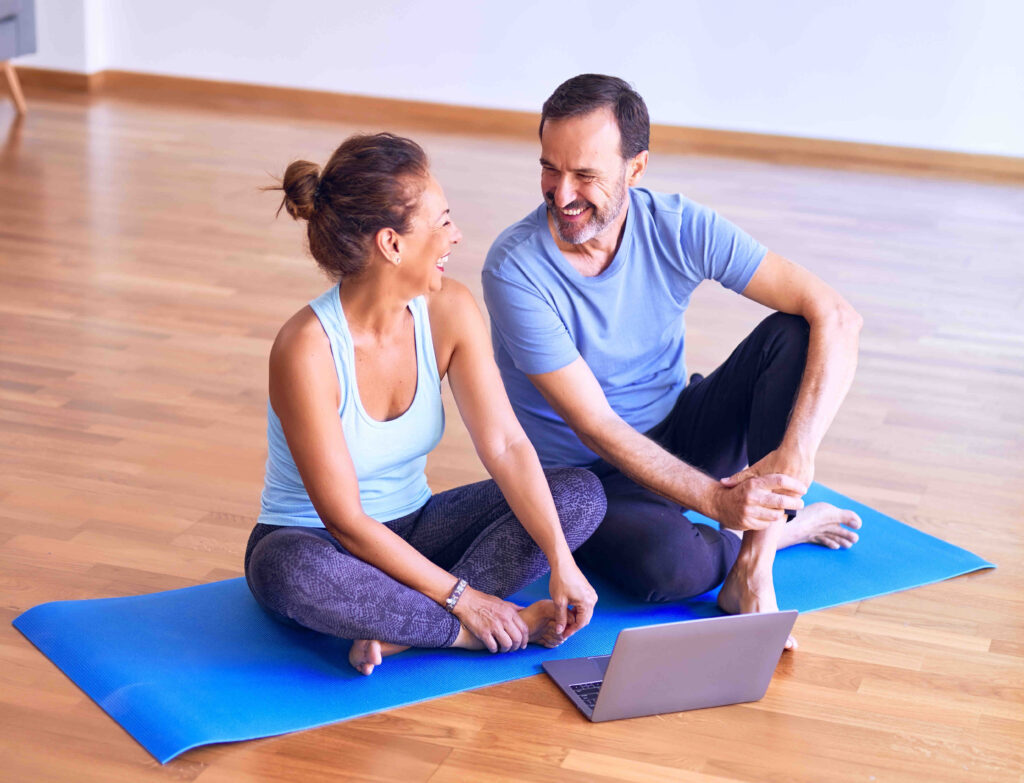 A couple in their thirties or forties laughing on a yoga mat.