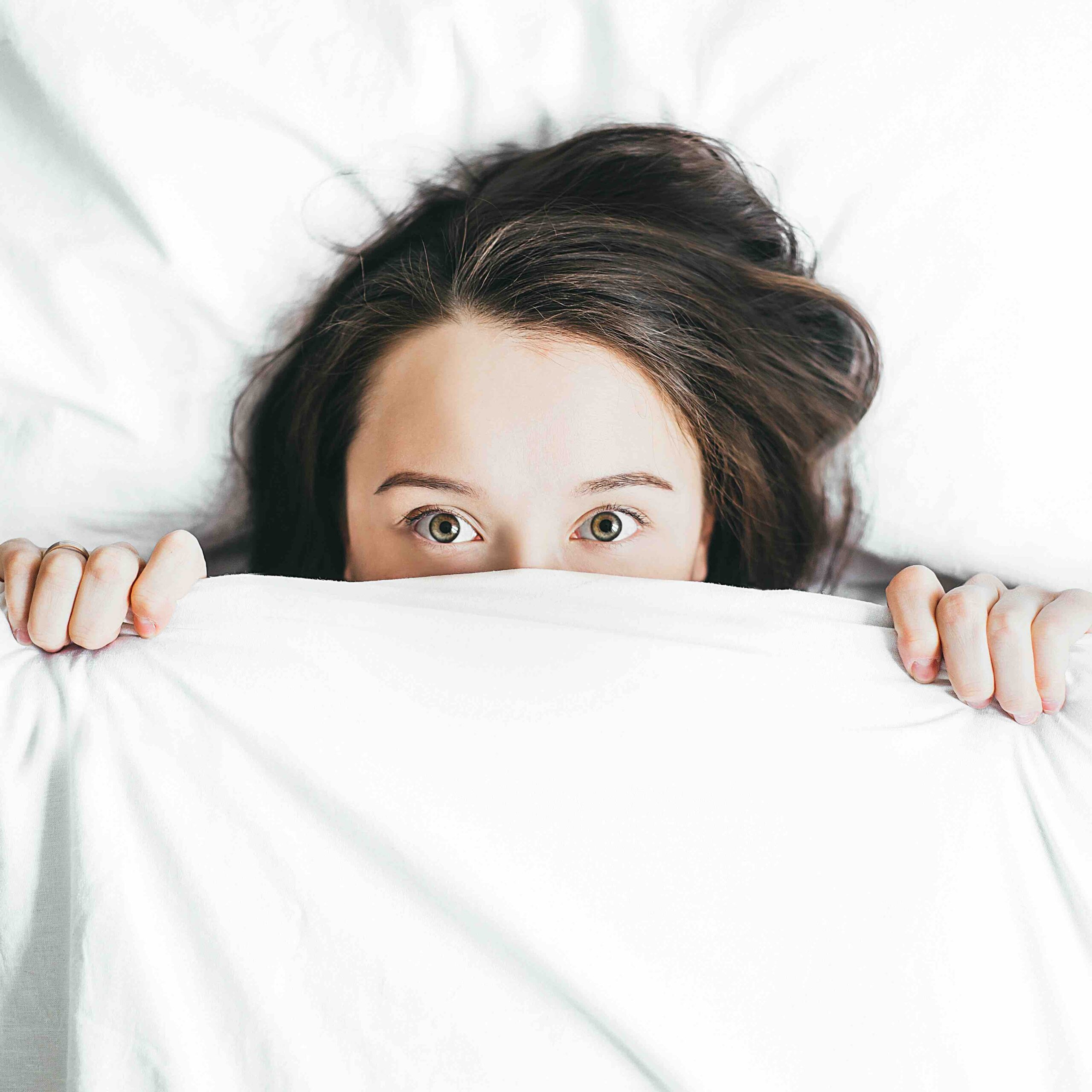 A woman in need of some sleep hacks lying wide awake under her bedsheets.