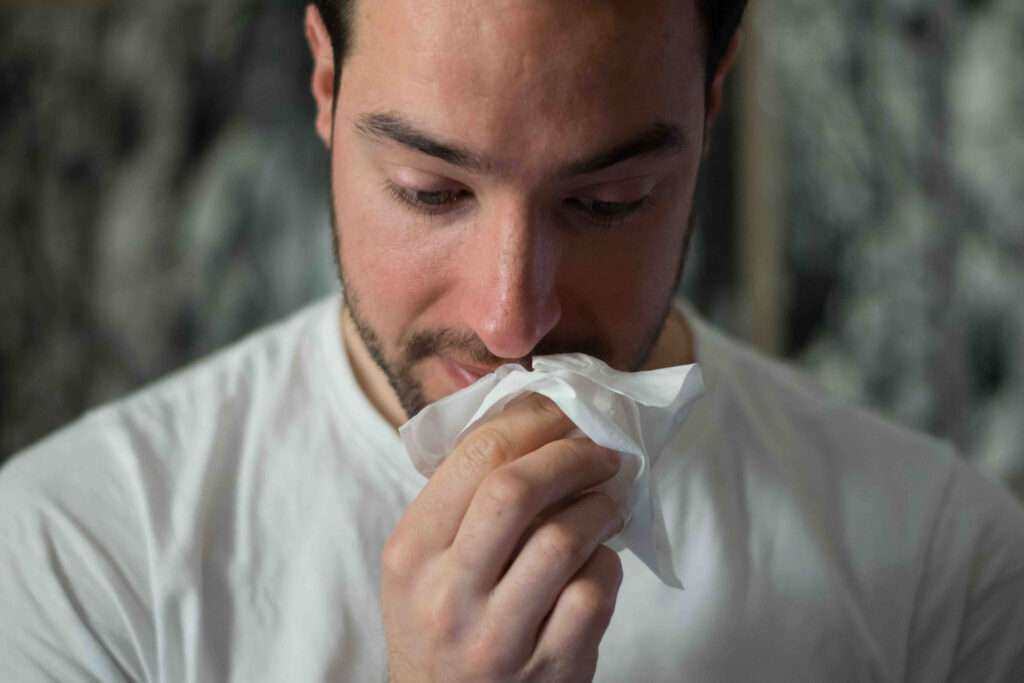 A man with a compromised immune system blows his nose into a tissue.