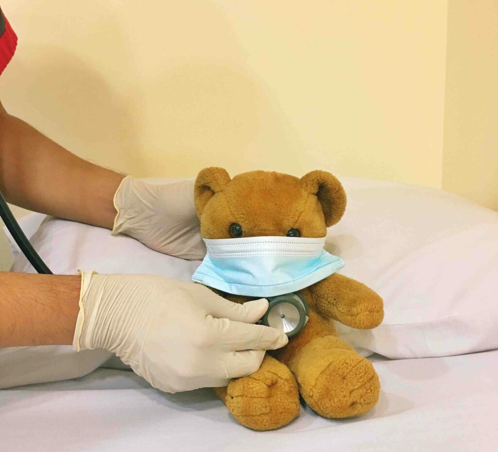 A teddy bear in a hospital bed getting an immunity booster shot.