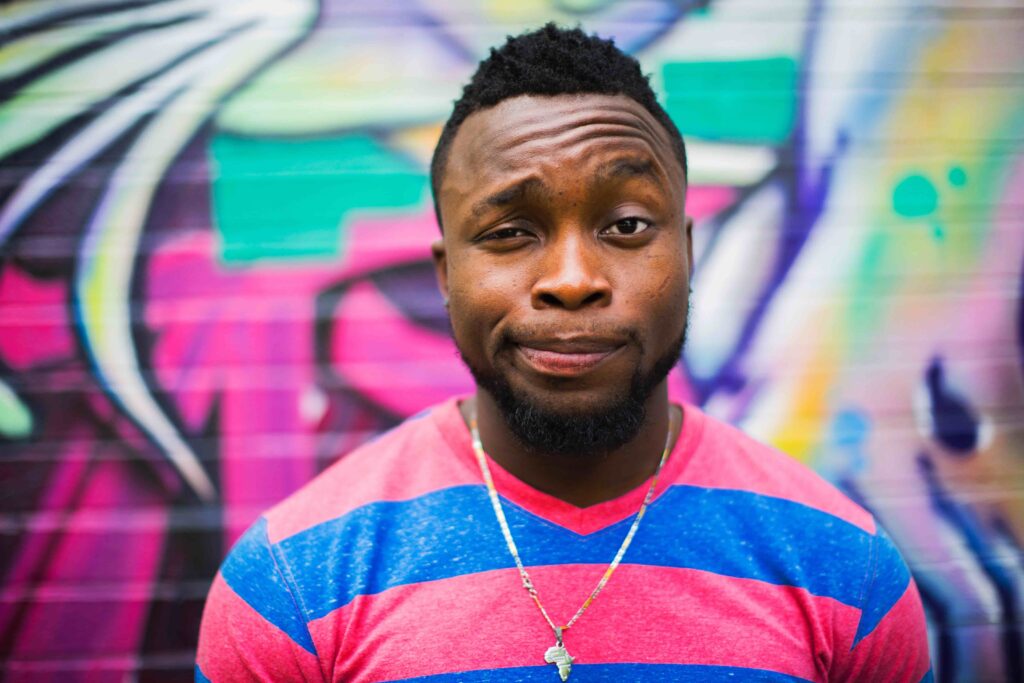 A guy making a quizzical face in front of a graffiti backdrop.