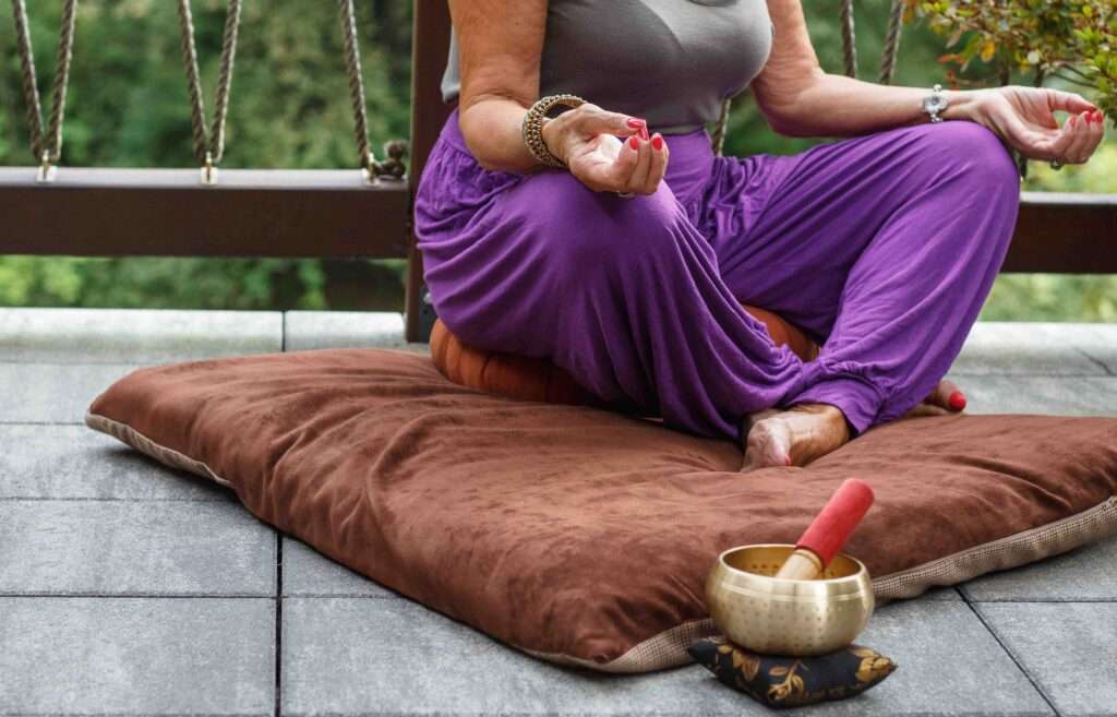 A woman meditating outdoors on a mat.