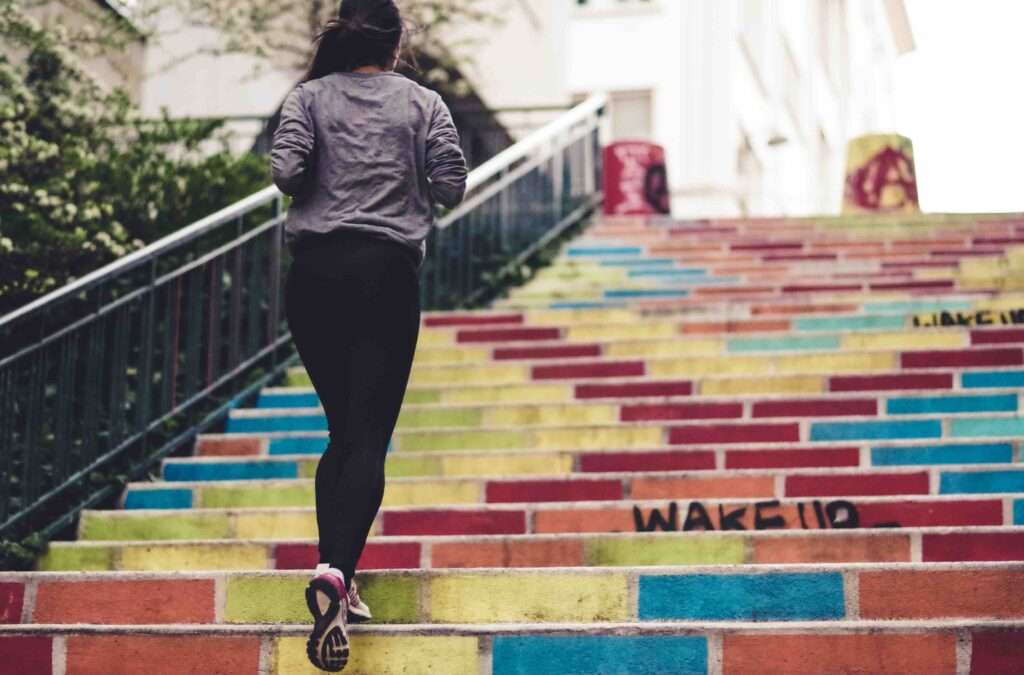 A woman running up a rainbow-colored set of outdoor stairs.