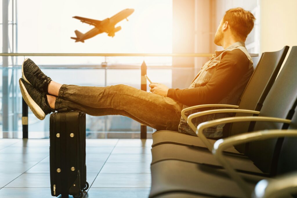 A man sitting in an airport terminal watching a plane take off.