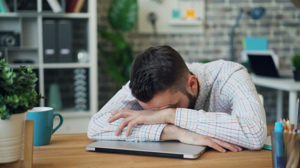 A man with his head down on his desk at work.