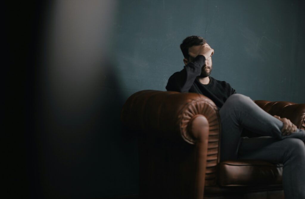 nik shuliahin BuNWp1bL0nc unsplash A man sitting on a couch with his face in his hands.